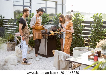 Happy young friends hanging out together, grilling food on a modern grill at beautiful backyard of a country house. People cooking food outdoors Royalty-Free Stock Photo #2011165250