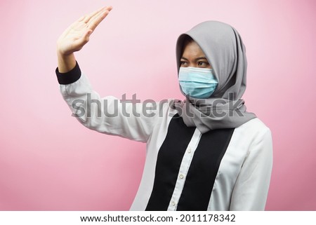 Muslim woman wearing medical mask with hand rejecting something, hand stopping something, hand disliking something, isolated on pink background