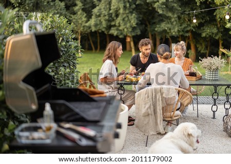 Small group of a young friends have a lunch outdoors, eating grilled vegetables and fish and having fun at backyard with grill