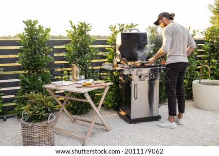 Man cooking on the modern gas grill at beautiful backyard on a sunset. Cooking food on the open air Royalty-Free Stock Photo #2011179062