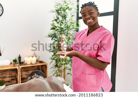 Young physiotherapist woman smiling happy holding oil massage at the clinic. Royalty-Free Stock Photo #2011186823