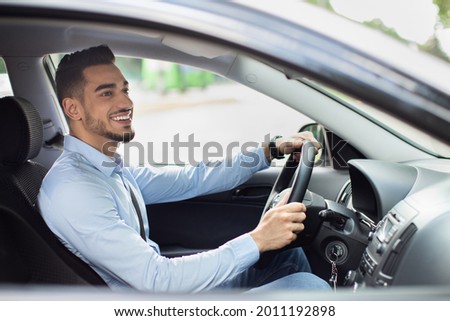 Excited arab guy going to office in the morning, driving his car, side view, copy space. Cheerful middle-eastern young man looking at the road, sitting inside luxury automobile, going home from job Royalty-Free Stock Photo #2011192898