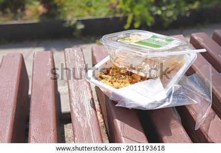 Leftovers food in disposable plastic package. Food left on a bench in plastic lunch boxes. Fast food. Lunch outdoor on a summer day. Plastic waste, plastic pollution. Consumerism. Food consuming. 