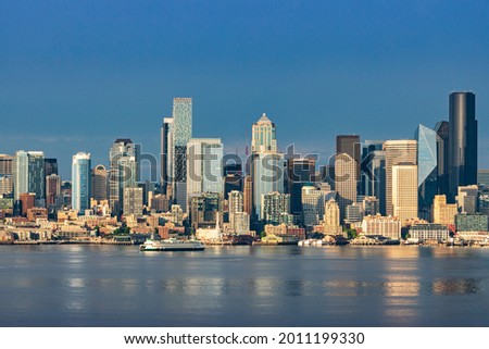 A Washington State Ferry crosses Elliott Bay as the downtown Seattle skyline rises above Puget Sound on a beautiful evening in the Pacific Northwest. Royalty-Free Stock Photo #2011199330