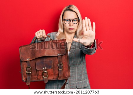 Beautiful caucasian blonde business woman wearing leather bag with open hand doing stop sign with serious and confident expression, defense gesture 