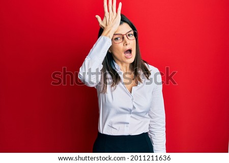 Young hispanic woman wearing business shirt and glasses surprised with hand on head for mistake, remember error. forgot, bad memory concept.  Royalty-Free Stock Photo #2011211636