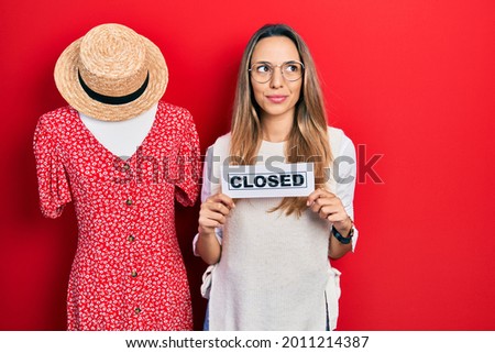 Beautiful hispanic woman holding closed business banner smiling looking to the side and staring away thinking. 