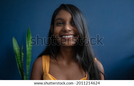 Image of a dark-skinned young carefree girl smiling towards the camera| happy teenage girl isolated on a blue studio background | Indoor lifestyle of a 20's teenage girl