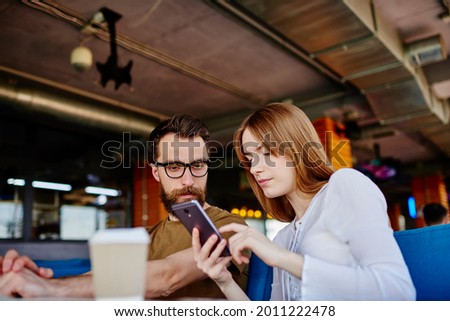 Millennial male and female users browsing web content via cellphone device connecting to 4g internet indoors, young friends discussing received email message while chatting in social networks