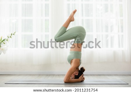 Side view of Asian woman wearing sportwear doing Yoga exercise in front of windows,Yoga Forearm Stand pose or Pincha Mayurasana.Calm healthy young female breathing and meditate yoga self care at home Royalty-Free Stock Photo #2011231754