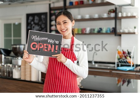 Portrait of woman owner standing at her coffee shop gate with showing open signboard
