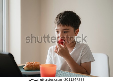 Healthy Child boy eating fresh strawberry and croissant , Happy kid watching cartoon on tablet while having breakfast. Children relaxing at home in morning, Healthy food and drink concept