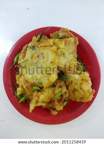 A plate of "bakwan" (a mixture of carrots, cabbage and wheat flour dissolved in water and cooked by frying) on ​​a red plate with sprinkle green chili.