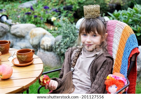 Adorable  brunette little girl playing outside in the autumn garden with her doll: having tea party