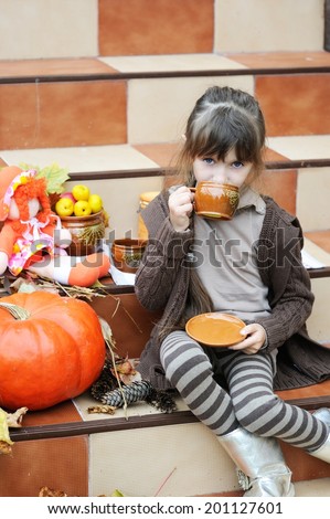 Little girl sitting outdoors on stairs with leaves and pumpkin 