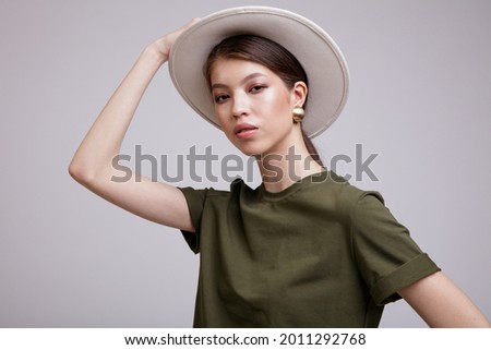 Fashion photo of a beautiful elegant young asian woman in a pretty green t-shirt, hat posing over white, soft gray background. Studio Shot. Portrait