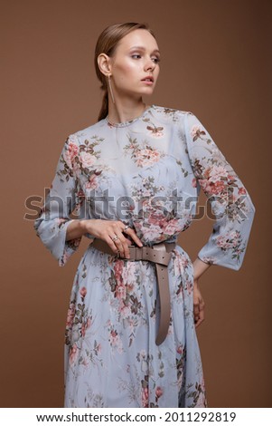 Fashion photo of a beautiful elegant young woman in a pretty blue pastel dress with a floral pattern, posing over brown coffee background. Studio Shot. Portrait