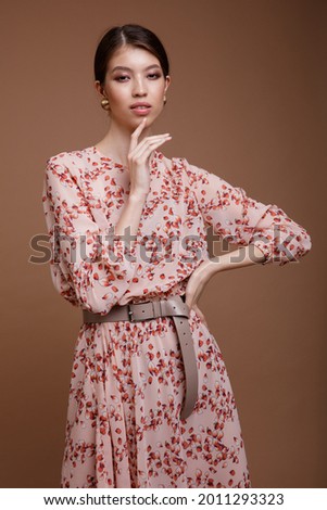 Fashion photo of a beautiful elegant young asian woman in a pretty beige dress with a floral pattern posing over brown coffee background. Studio Shot. Portrait