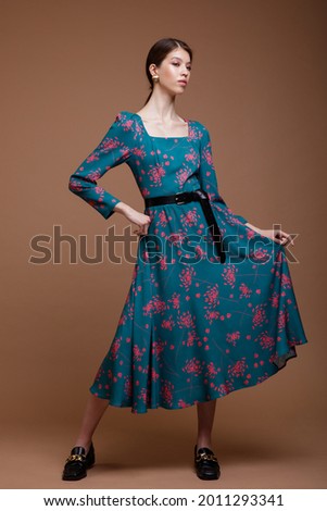 Fashion photo of a beautiful elegant young asian woman in a pretty blue ocean color dress with a floral pattern posing over brown coffee background. Studio Shot. Portrait