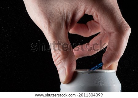 A man's hand opening a soda can on a black background and showing the splash when opening the can. Royalty-Free Stock Photo #2011304099