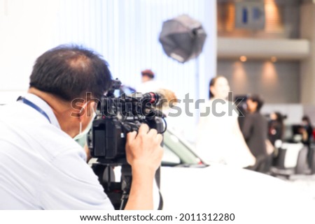 A Video cameraman or video photographer with recording shooting with car in the exhibition event in the conference event hall with car blurred background.