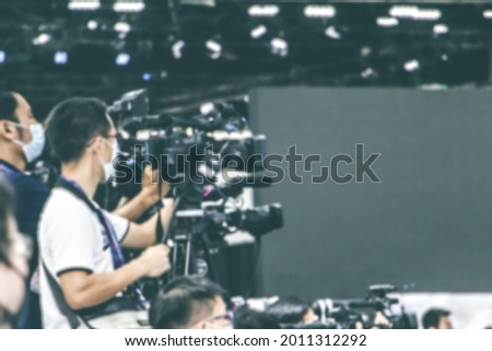 Blurry Video cameraman or video photographer with recording shooting of grand opening product event in the conference event hall with blurred background. Concept of live streaming and event.