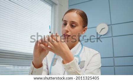 Blonde young woman medical blogger in white coat shows syringe in hospital