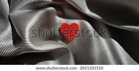 Small red patterned heart in folds of striped silk (top view).