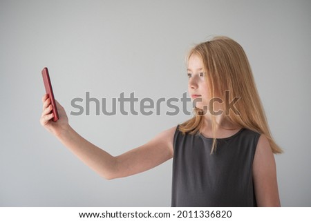 a girl in gray dress  and with a  phone on the gray background  takes photos