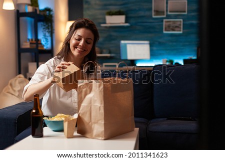 Smiling cheerful woman unpacking tasting fast-food home delivered sitting on couch having lunch serivce order. Caucasian female enjoying delicious takeaway delivery tasty meal in evening Royalty-Free Stock Photo #2011341623