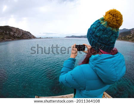 A girl photographs the sea on a smartphone, a woman travels along the coast in the cold season, a girl in a hat against the backdrop of a beautiful lake, sights of Turkey.