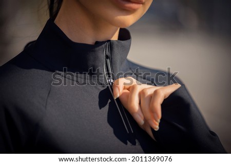 Frontal view of close up photo of happy unknown female tying up the zipper. She is wearing black termal active wear. City on background.
