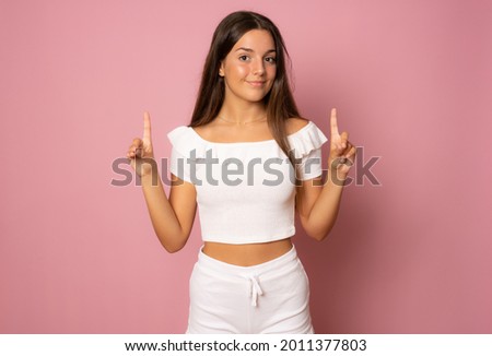 beautiful girl pointing fingers up isolated over pink background.