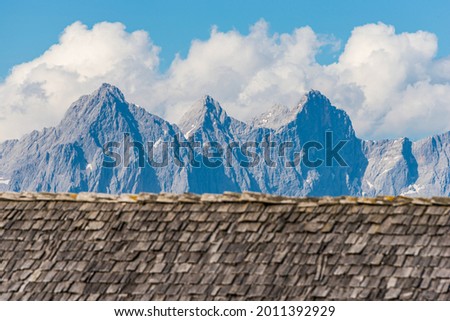 Blured weathered and faded from the sun, rain and snow wooden shingles that are the roof of an alpine house against the backdrop of high alpine mountains. Wooden texture in shades of gray and orange.