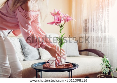 Woman puts vase with pink lily flowers on table. Housewife taking care of coziness at home. Interior and summer decor Royalty-Free Stock Photo #2011398116