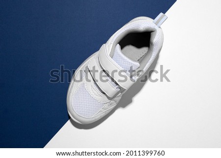 top view macro on one white children's running shoe with velcro fasteners for quick shoeing on a trendy blue and white paper background with a hard light.
