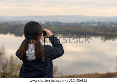 Image of a girl looking through binoculars with a lake in the background.