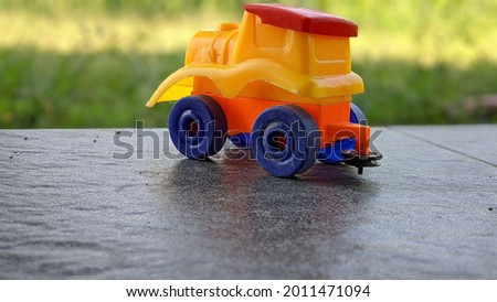 A toy locomotive parked on the edge of the tiled floor and near the grass.