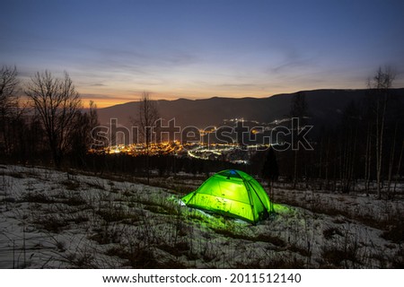 Tent in the winter in the mountains with a view of the night city in the Carpathians