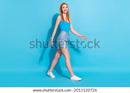 Photo portrait red haired woman in pretty singlet jeans skirt walking forward isolated pastel blue color background