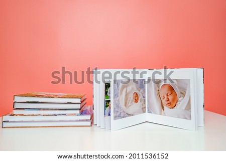 on a pink background a photobooks. open photo album from photo shoot with a newborn child. traditions to make a photo album and print photos from important moments of life.