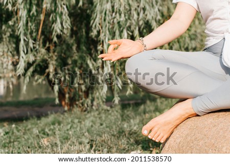 Meditation in nature. Close-up of meditating yoga woman sitting on stone in lotus position outdoors. Woman's hand folded in asana for meditation, copy space. Healthy lifestyle, restoration of vitality Royalty-Free Stock Photo #2011538570