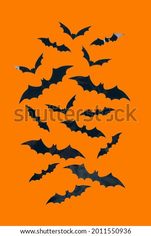 Halloween background - decorative paper bats on orange background with copy space. Halloween decorations or party invitation concept. Selective focus, vertical image