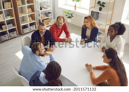 Team of happy business people discussing funny positive stuff in group meeting. High angle shot of diverse corporate company employees and coworkers sitting together around office table and talking Royalty-Free Stock Photo #2011571132