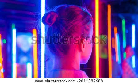 Back view - portrait of woman looking right at interactive exhibition or museum with colorful fluorescent tube illumination. Futuristic, retrowave, immersive, entertainment concept Royalty-Free Stock Photo #2011582688