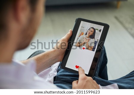 Finding love on modern online dating website or mobile app: Man looking at profile pic of pretty young woman on digital tablet display gives her like and sends her message. Close up, closeup shot