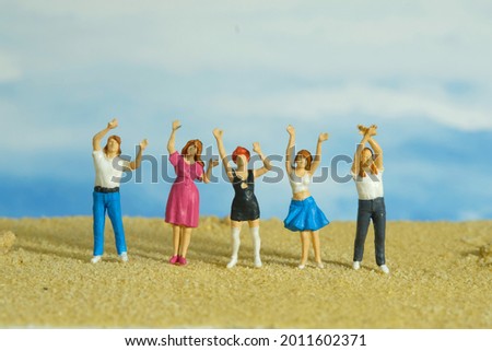 Miniature tiny people toys photography. Group of teens raised hand or hands up celebration at the beach. Image photo