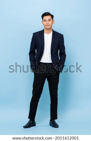 Full length portrait of young handsome Asian businessman standing and posing with hands in pockets on light blue studio background Royalty-Free Stock Photo #2011612001