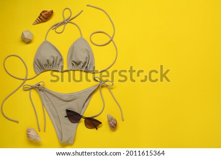 Stylish beige bikini, sunglasses and seashells on yellow background, flat lay. Space for text