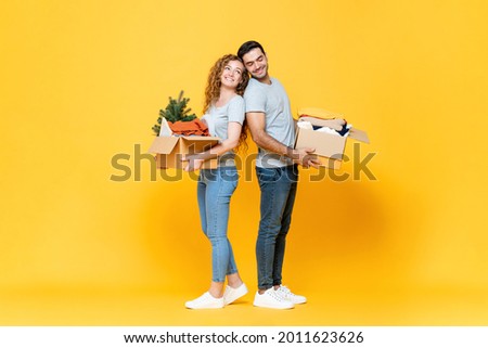 Happy interracial couple carrying stuff in yellow studio isolated background, moving house concept